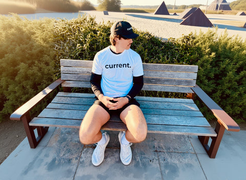 Person sitting on a bench wearing a 'current.' shirt in an outdoor setting.